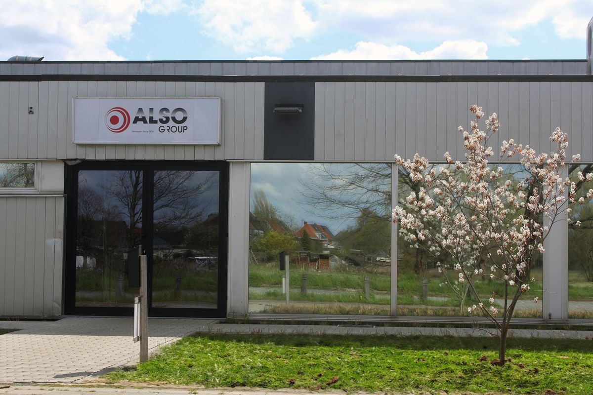 Voorgevel van het gebouw van ALSO Group met uithangbord en een bloeiende boom op de voorgrond